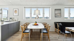 Een moderne keuken met een eethoek, grote ramen en uitzicht op zee.