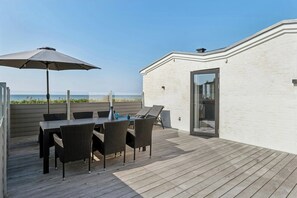 Eine Terrasse mit Tisch, Stühlen, einem großen Sonnenschirm und einer Glastür zum Gebäude.