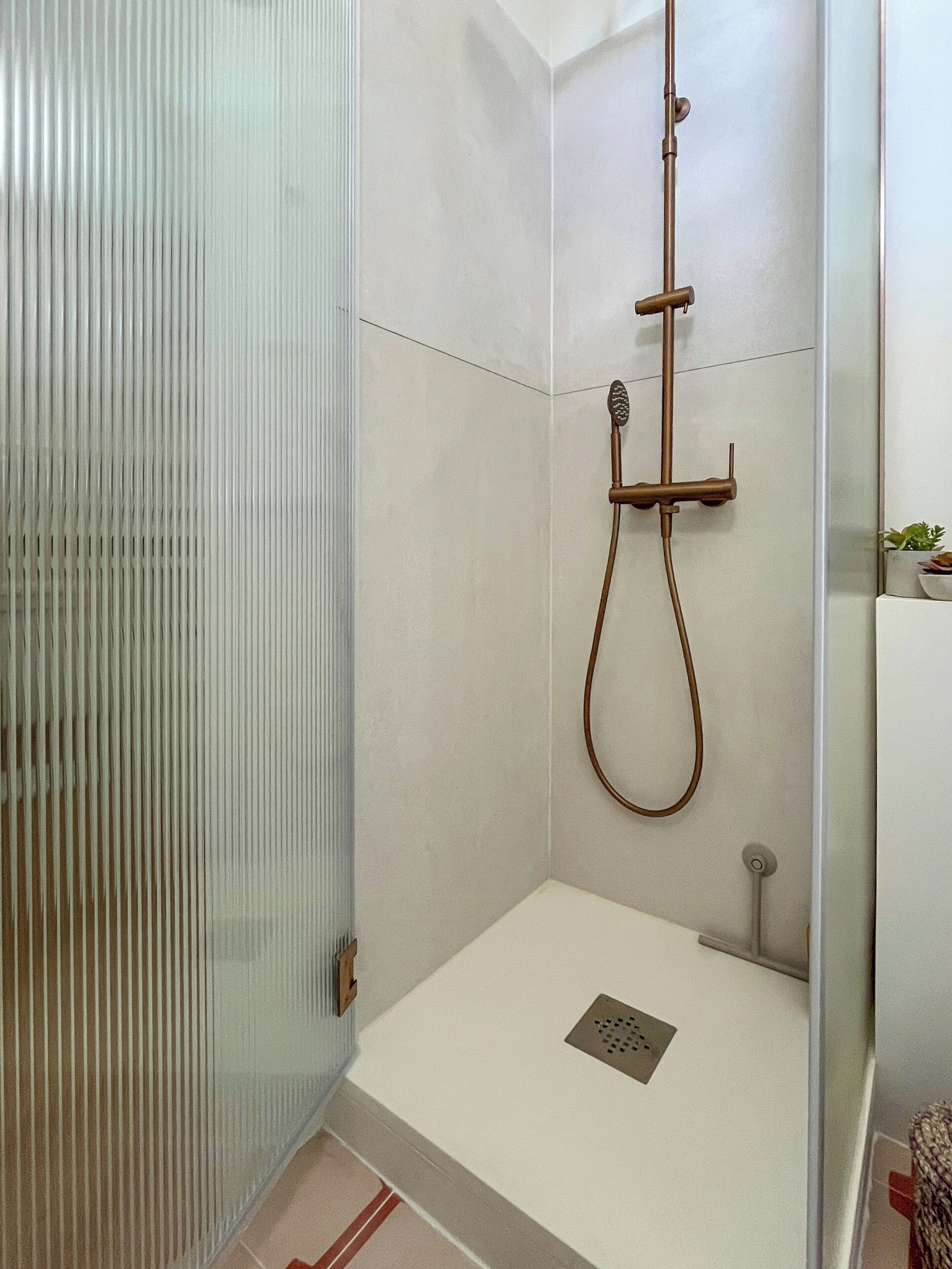 A modern bathroom with a glass shower enclosure, a handheld showerhead, and a small sink.