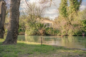 Blick auf einen Fluss mit einem Haus, Bäumen und einem Wasserrad.