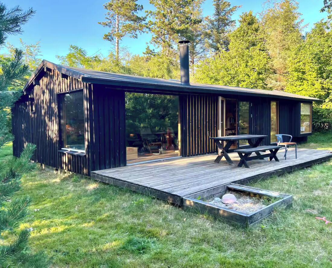 A modern wooden cabin with a deck, a table, and a bench.