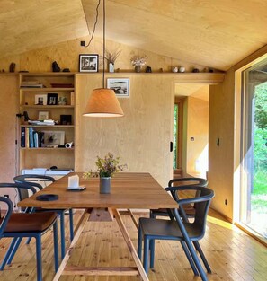Ein Holzinterieur mit Esstisch, Stühlen, Bücherregalen und einer Pendelleuchte.