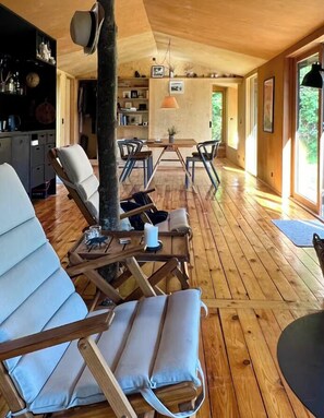 Ein geräumiges Zimmer mit Holzboden, einer Essecke mit Tisch und Stühlen sowie einem großen Fenster, das für natürliches Licht sorgt.