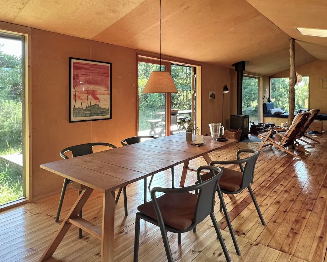 Een houten eettafel met stoelen, een hanglamp en een schilderij aan de muur.