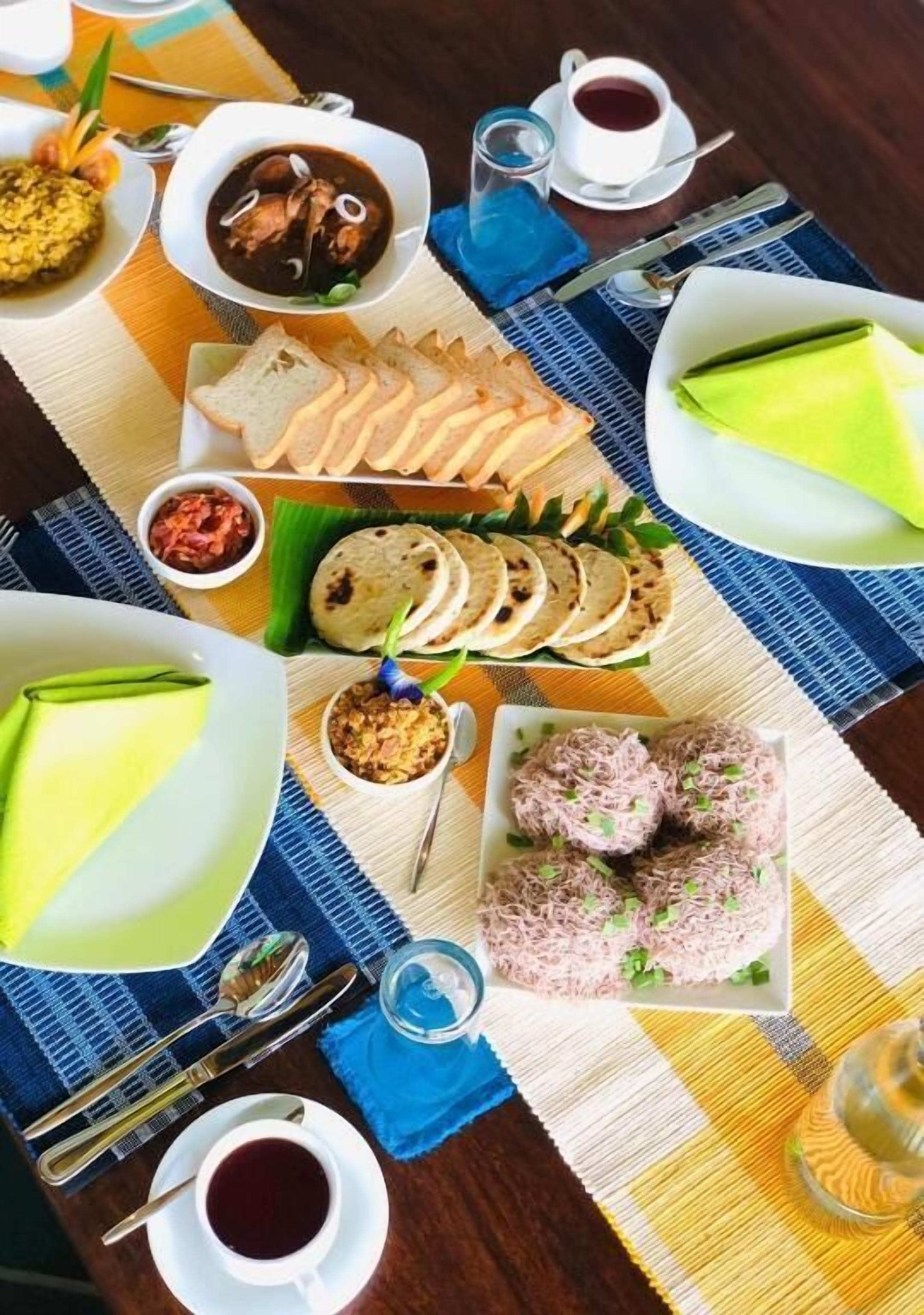 A table with various dishes, including a green dessert, a soup, and a plate of pink rice balls.