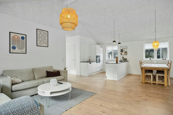 Een moderne woonruimte met een bank, salontafel, eettafel, keuken en kunstwerken aan de wanden.