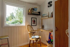 Una habitación con ventana, una silla, estanterías con libros y un cuadro enmarcado, y una puerta.