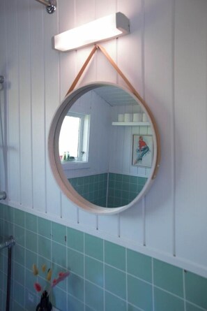 Une salle de bain avec un miroir rond, une fenêtre et un mur recouvert de carreaux.
