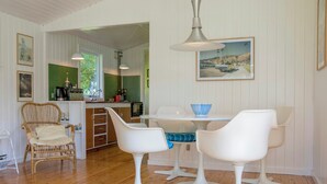 Een eethoek met een witte tafel en stoelen, een hanglamp en een schilderij aan de muur.