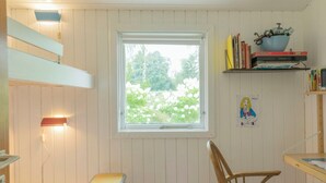 Een kamer met raam, een stoel, een klein krukje, een plank met boeken en een schaal, en een wandlamp.