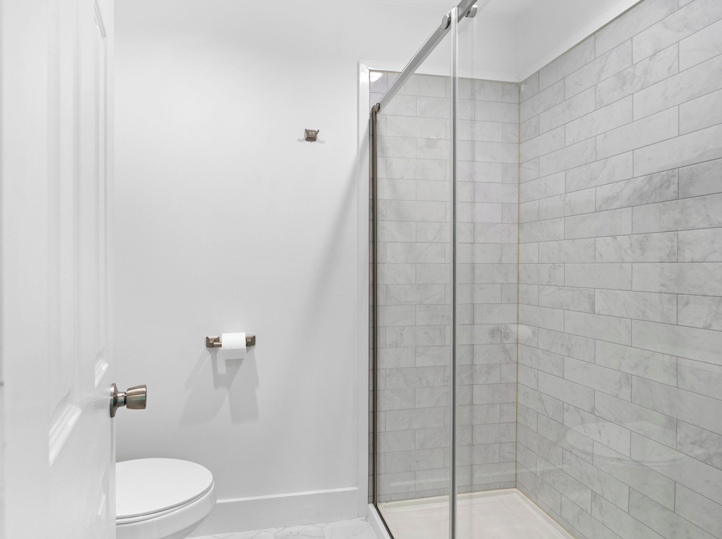A bathroom with a toilet, a glass shower enclosure, and a marble-tiled wall.