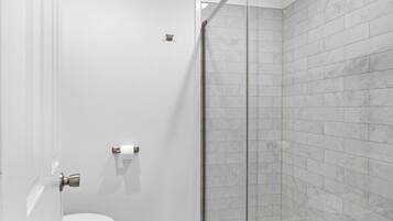 A bathroom with a toilet, a glass shower enclosure, and a marble-tiled wall.