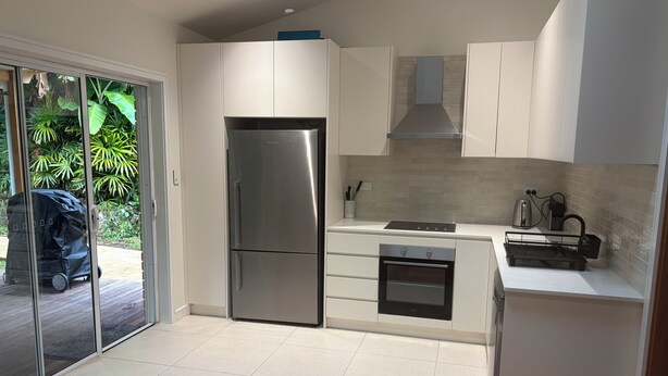 Una cocina moderna con armarios blancos, un refrigerador de acero inoxidable, horno empotrado y estufa a gas.