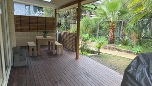 Una terraza de madera con una mesa y sillas, rodeada por una valla de bambú y abundante follaje.