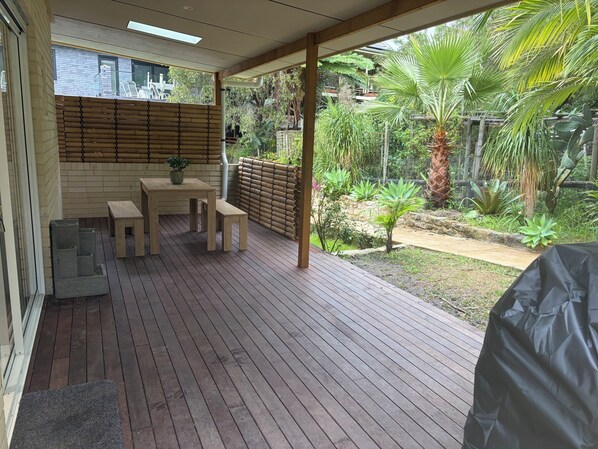A wooden deck with a table and chairs, surrounded by a bamboo fence and lush greenery.
