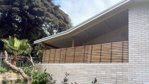 Un edificio con fachada de ladrillo blanco, un patio cubierto y una valla de bambú.