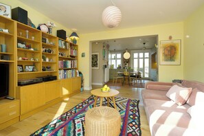 Uma sala de estar com sofá, mesa de centro, estante e área de jantar ao fundo.