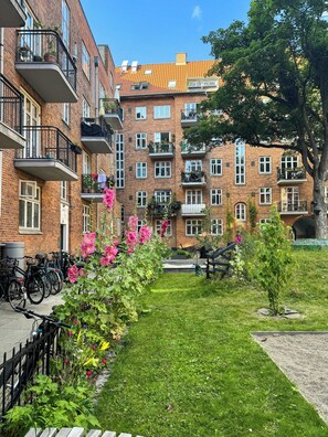 Un immeuble en briques à plusieurs étages, doté de balcons, d’une cour verdoyante et de vélos garés à l’extérieur.