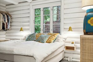 Ein Schlafzimmer mit einem Bett, Nachttischlampen, einem Schminktisch und einem Fenster mit Blick ins Grüne.