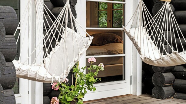 Two white macramé hammocks hanging from wooden beams, a window with a view of greenery, and a wooden door. - Scenic and idyllic log summer house by Arresø (Frederiksværk)