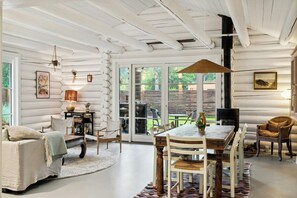 Ein Interieur einer Blockhütte mit Essbereich, Kamin und Blick durch Glastüren.