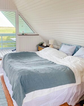 Ein Schlafzimmer mit einem großen Bett, einem Nachttisch, einer Lampe und einem Fenster mit Blick auf eine Wiese.