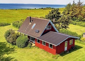 Ein rotes Haus mit einem geneigten Dach, einem Schornstein und Blick auf das Meer.