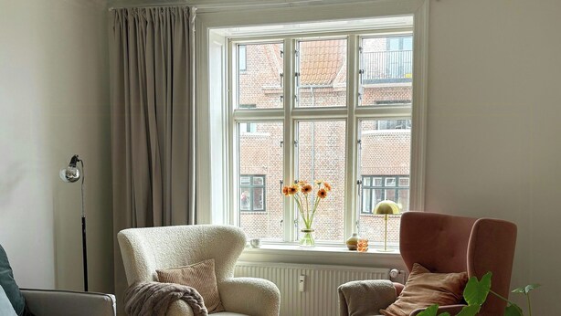 Un salon comprenant un canapé, deux fauteuils, une table basse, un lampadaire et une fenêtre donnant sur des immeubles.
