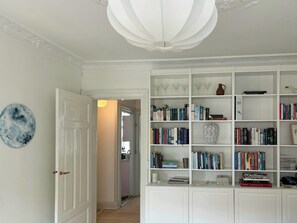 Ein Flur mit einer weißen Tür, einer weißen Decke mit einer dekorativen Leuchte und einem weißen Bücherregal, das mit Büchern und Dekoration gefüllt ist.