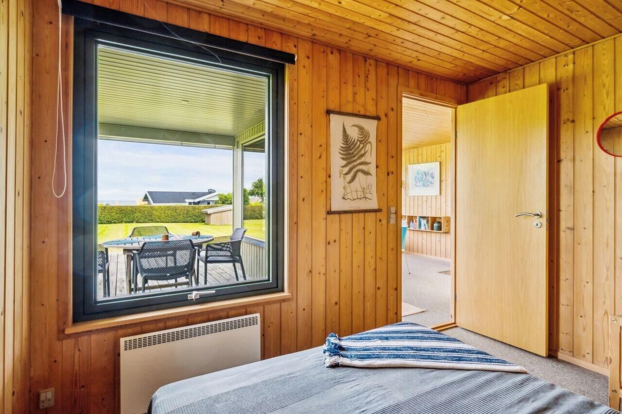 Een kamer met houten lambrisering, een bed, een raam met uitzicht en een kunstwerk in een lijst, plus een deur.