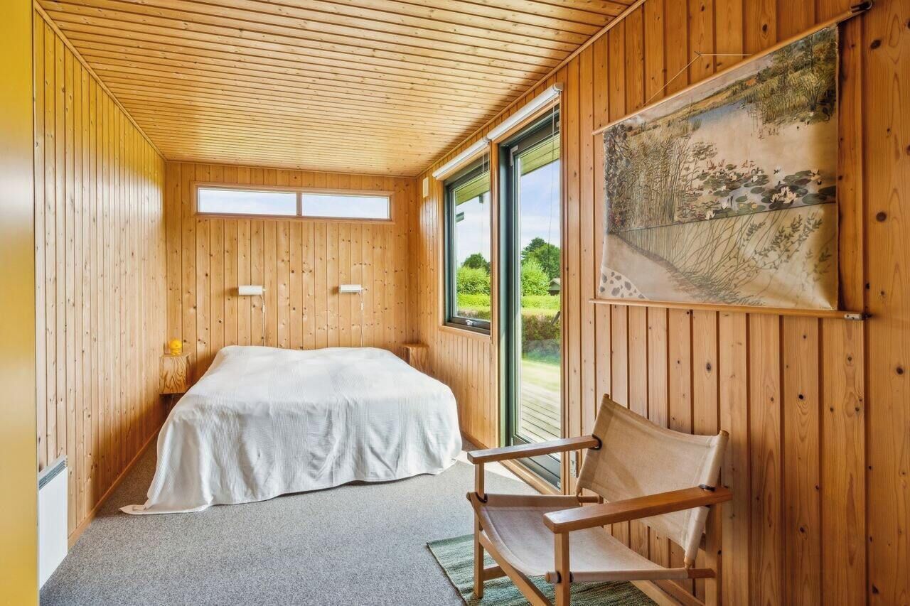 A wooden-paneled room with a bed, a chair, and a large window.