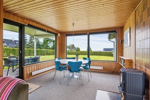 Un espace extérieur abrité, aménagé pour les repas, avec une table et des chaises, une grande fenêtre et un plafond lambrissé.