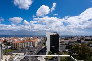 Eine Stadtlandschaft mit einem markanten, modernen Gebäude, einer breiten Straße mit einem Stoppschild und im Hintergrund freie Sicht auf das Meer.