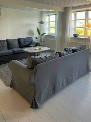En moderne stue med en grå sofa, et lille rundt bord og en potteplante.