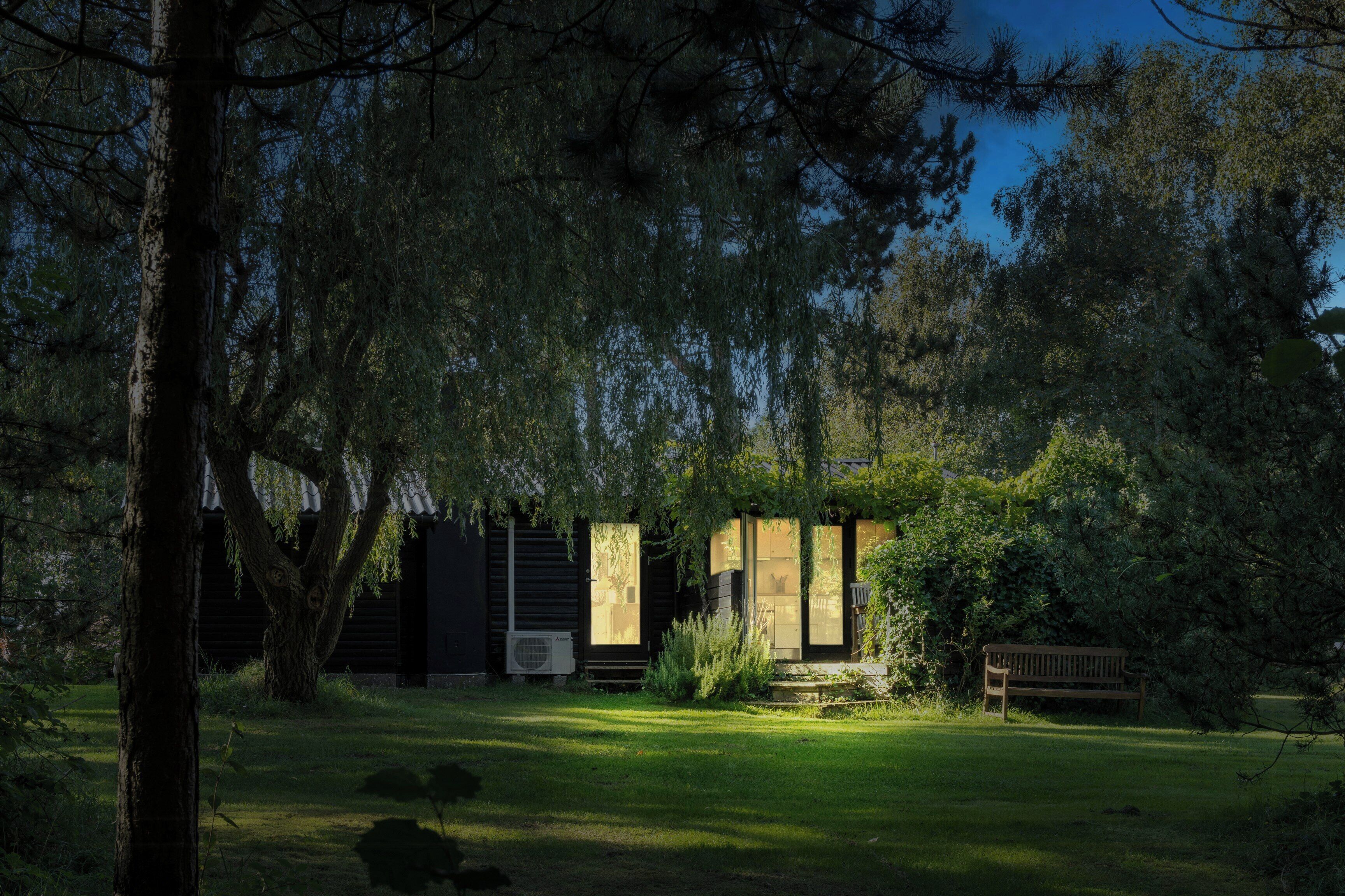 A secluded cabin with a wooden deck, surrounded by dense trees and a well-maintained lawn.