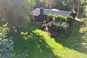 Ein Haus mit geneigtem Dach, umgeben von üppiger Vegetation und einem kleinen Garten.