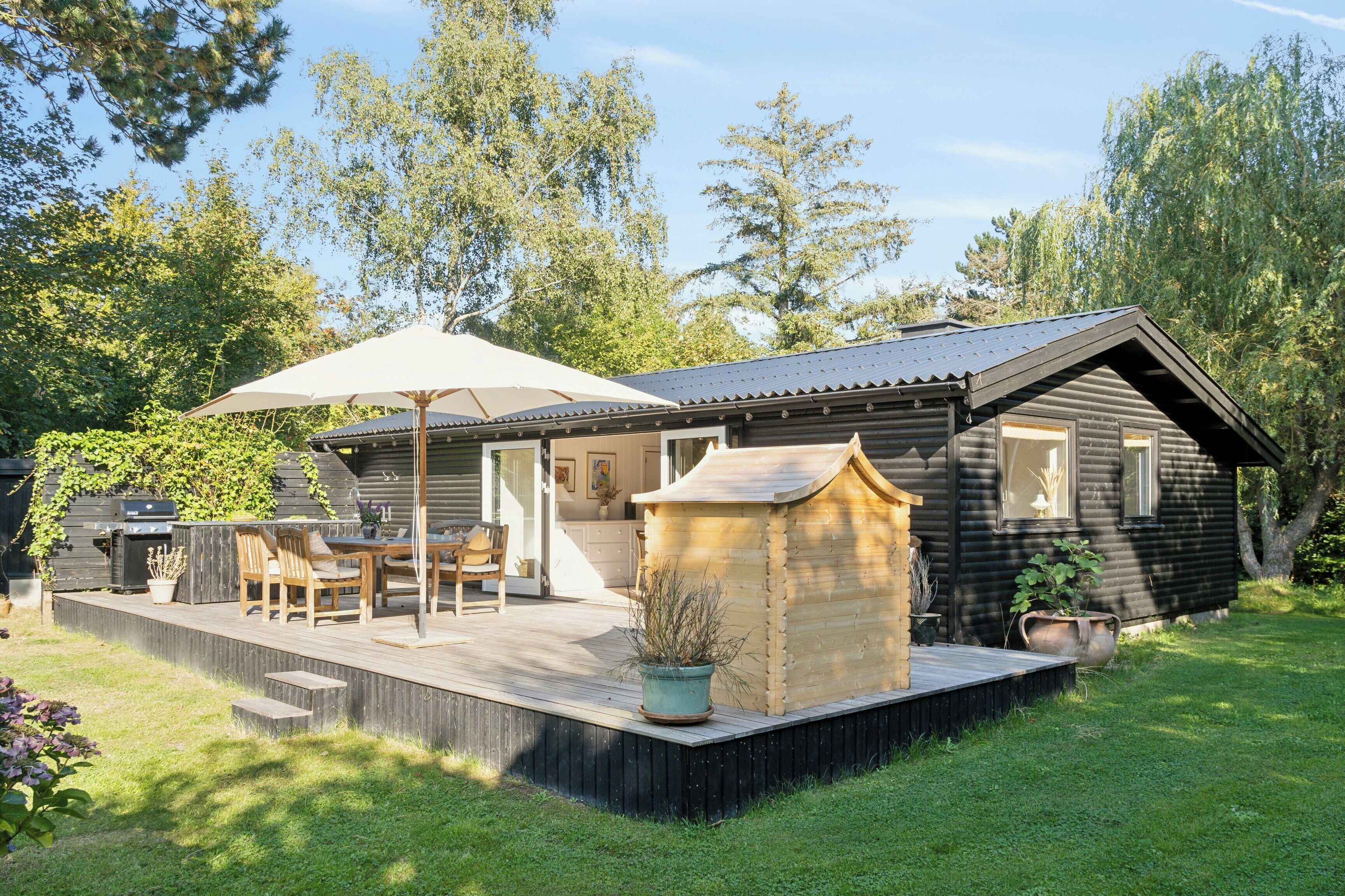 A log cabin with a deck, outdoor seating, and a small wooden structure.