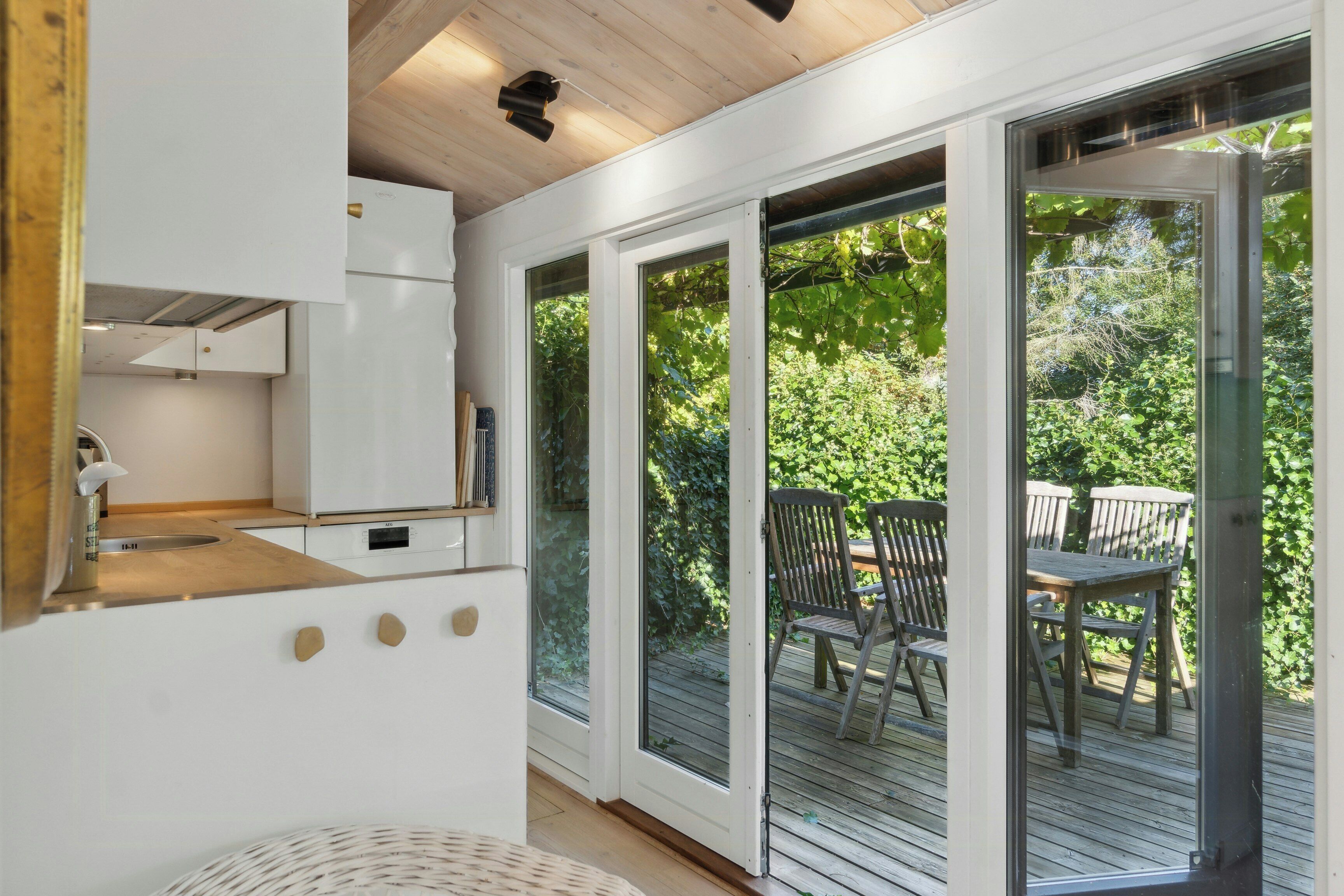 A modern kitchen with white cabinets, a wooden countertop, and a sliding glass door leading to an outdoor deck with a table and chairs.