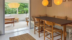 Een eetgedeelte met een houten tafel en stoelen, een bankje, en uitzicht op groen.