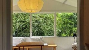 Een kamer met een houten tafel, een bank en een groot raam met uitzicht op groen.