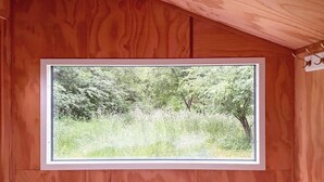 Een slaapkamer met een groot raam, houten wanden en een bed met een witte dekbedovertrek.