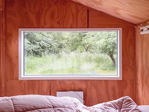 A bedroom with a large window, wooden walls, and a bed with a white comforter. - Nature-rich 60s holiday home by Isefjord (Jægerspris)