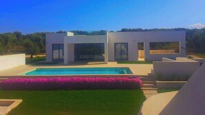Una casa moderna de dos pisos con piscina, rodeada por un jardín cuidado y vistas despejadas del paisaje.