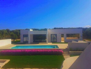 Ein modernes, zweistöckiges Haus mit Swimmingpool, umgeben von einem gepflegten Garten und freiem Blick auf die Landschaft.