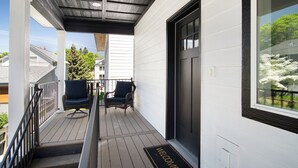 Une terrasse en bois avec une rambarde noire, deux chaises et une porte noire dotée d’une fenêtre.