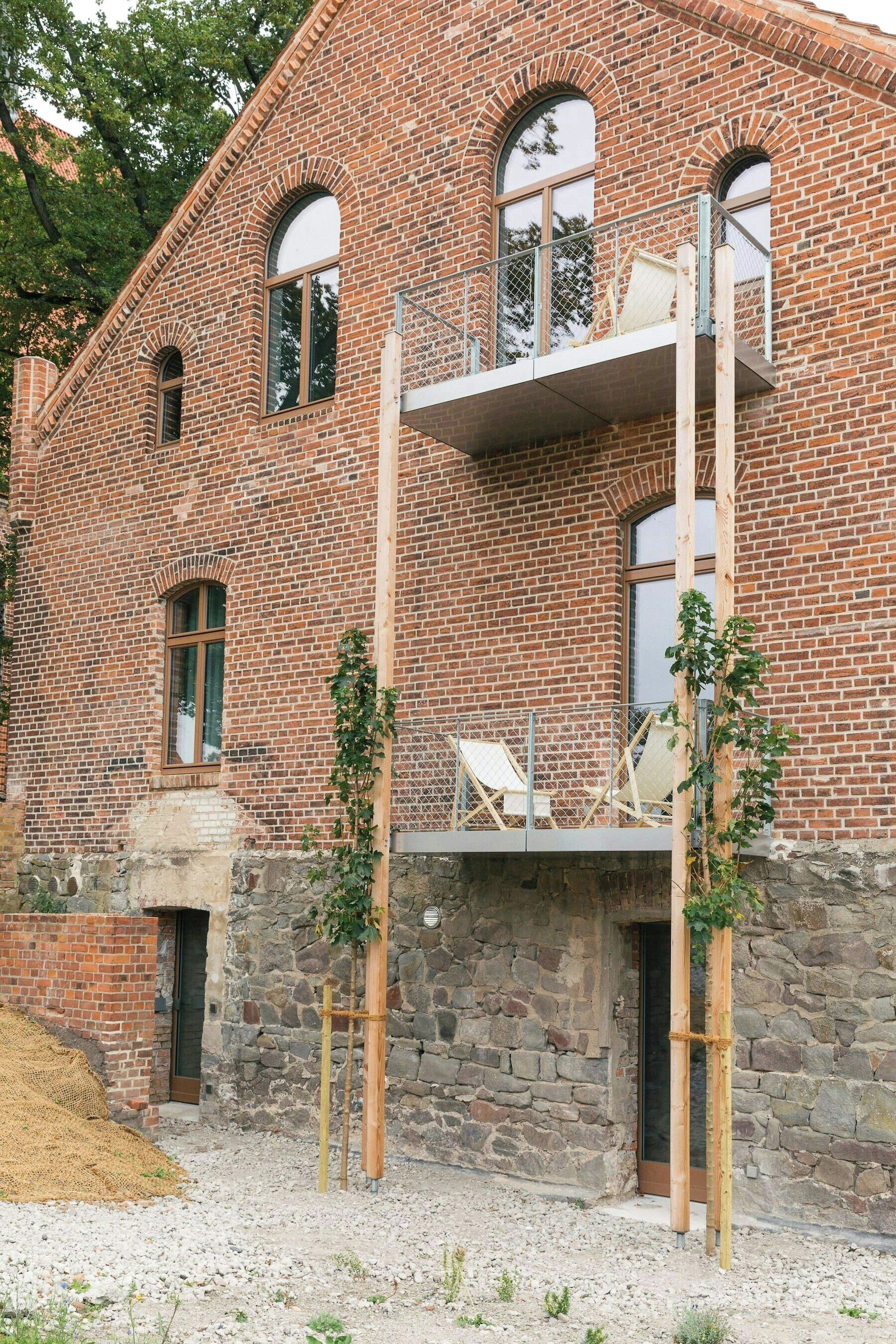 Ein Backsteinhaus mit Balkon, Steinuntergrund und einer hölzernen Struktur davor.