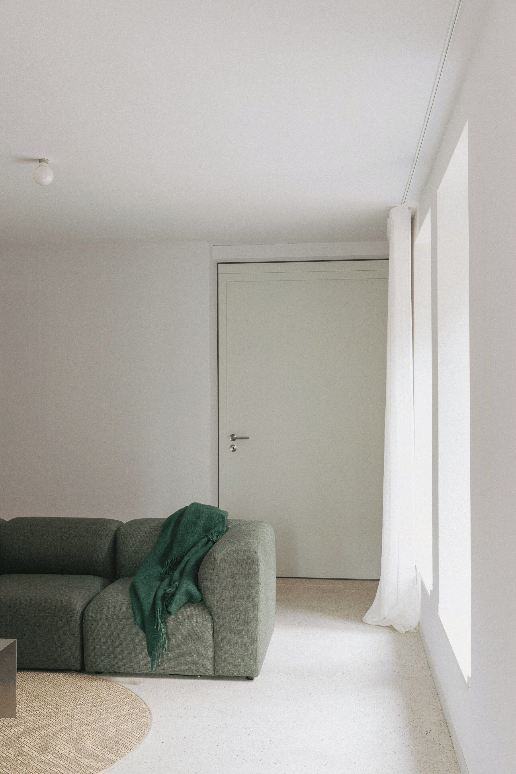 Un salon minimaliste avec un canapé, une porte et une fenêtre.