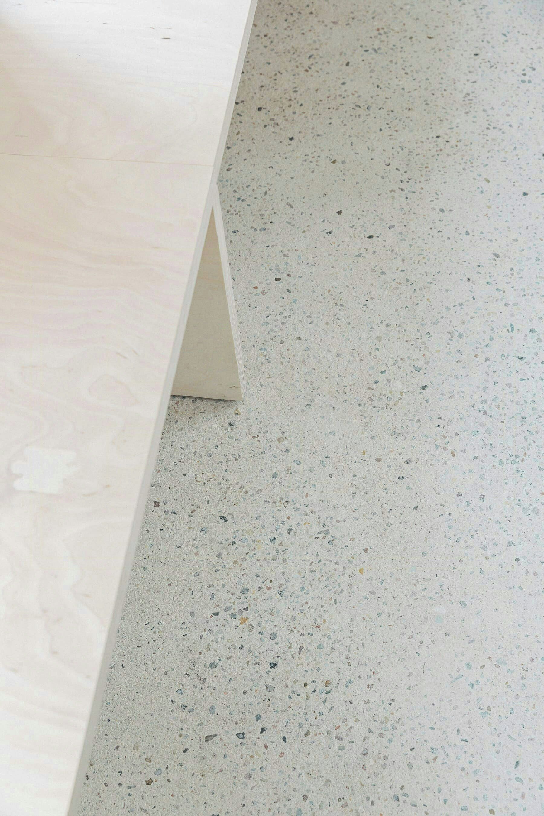 A corner of a room with a light-colored wooden table and a speckled floor.