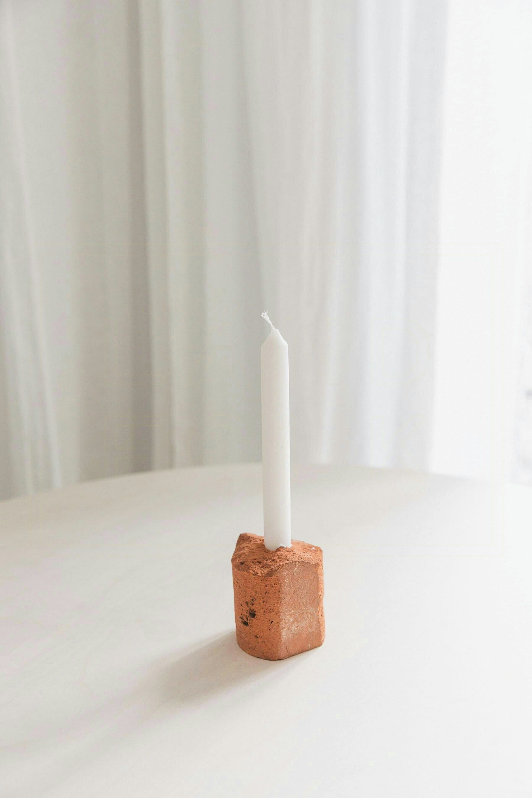 Une bougie blanche posée sur un socle en briques.