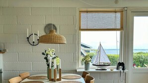 Ein Essbereich mit einem runden Tisch, Korbstühlen und Meerblick durch ein Fenster.